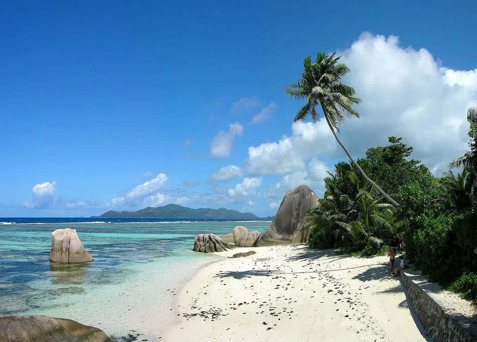 Rundgeschliffene Granitfelsen, Palmen und flaches türkisfarbenes Wasser an der Anse Source d'Argent auf La Digue