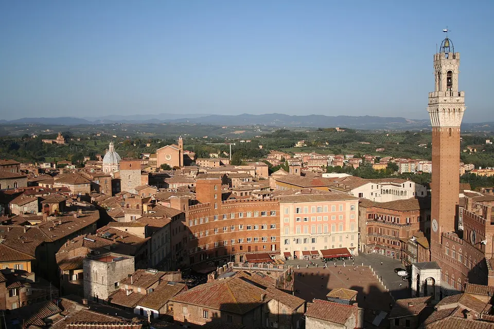 Siena: A photograph taken of the Piazza del Campo in Siena with tower Torre del Mangia and landscape with hills in background.